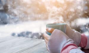 nainen lämmittää kylmiä käsiään kuuman teekupin ääressä.